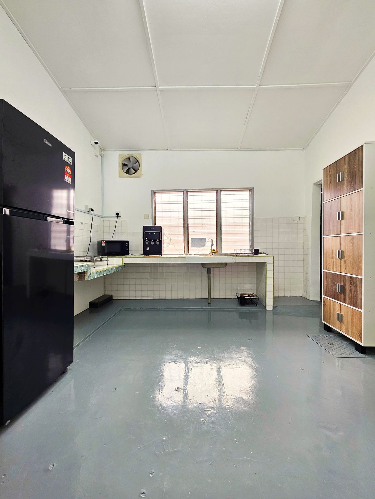 Shared kitchen with a fridge, microwave, water dispenser, tiled counter, and wooden cabinet